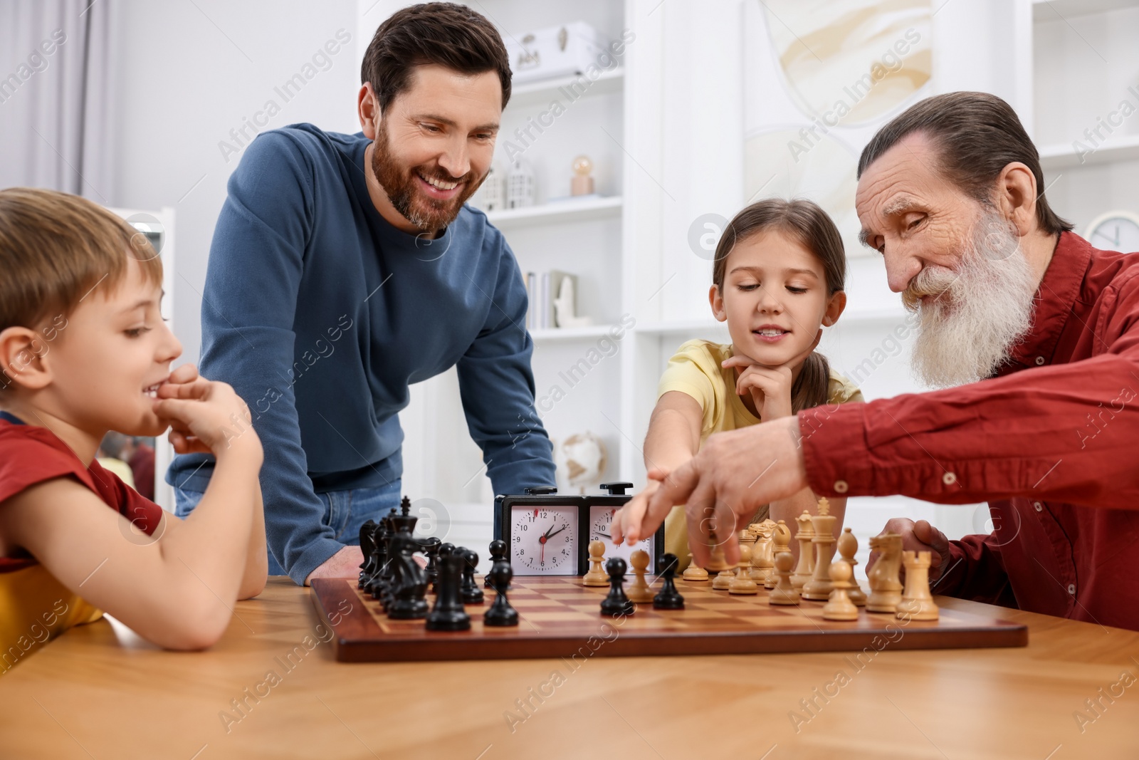 Photo of Family playing chess together at table in room