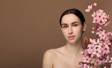 Image of Beautiful woman with smooth skin and flowers on brown background. Space for text