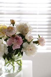 Photo of Beautiful peonies in vase on table near window indoors