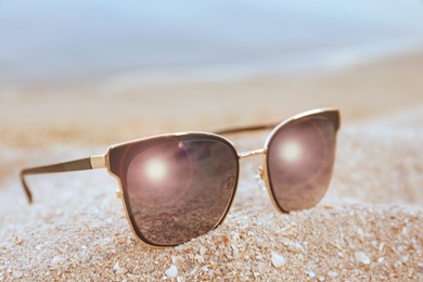 Photo of Stylish sunglasses on sandy beach, closeup view