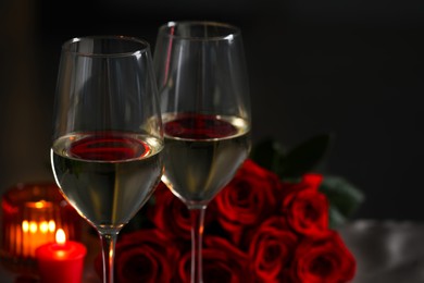 Photo of Glasses of white wine, burning candles and rose flowers against blurred background, space for text. Romantic atmosphere