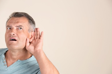 Photo of Mature man with hearing problem on light background. Space for text