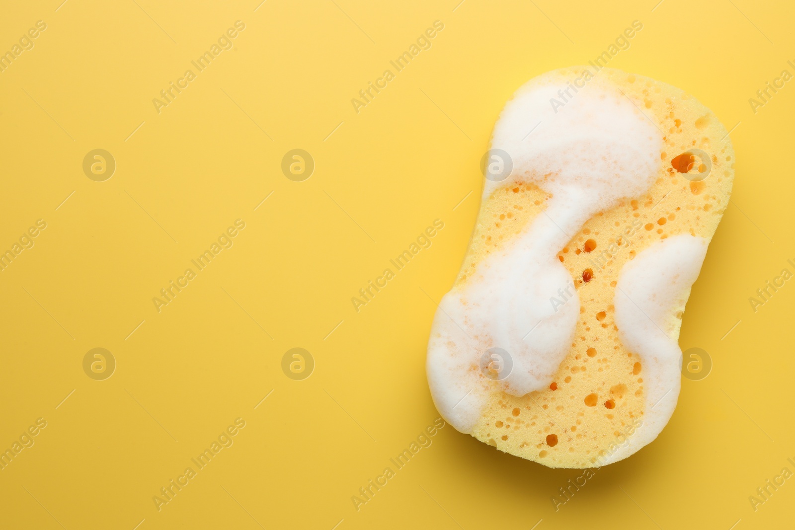 Photo of Sponge with foam on yellow background, top view. Space for text