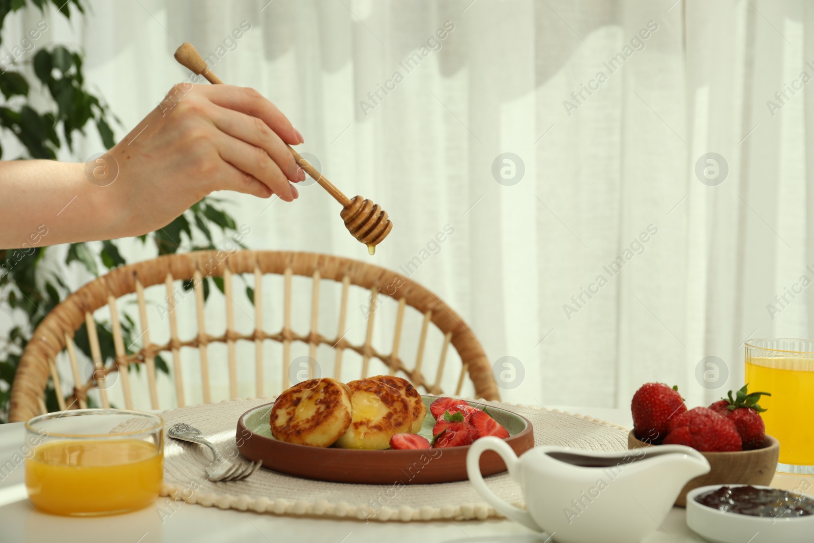 Photo of Woman pouring honey onto delicious cottage cheese pancakes at white table indoors, closeup