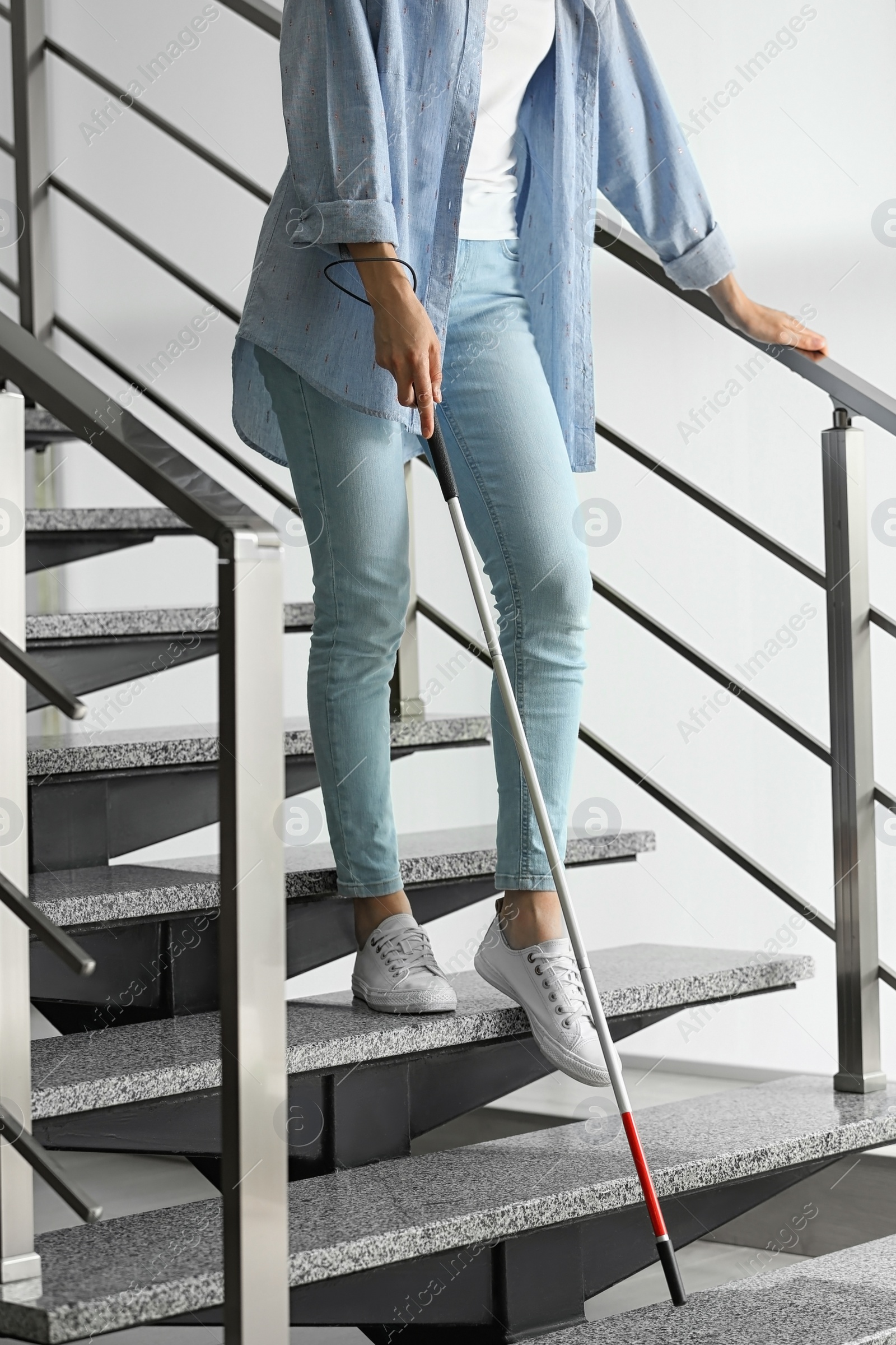 Photo of Blind person with long cane going down stairs indoors, closeup