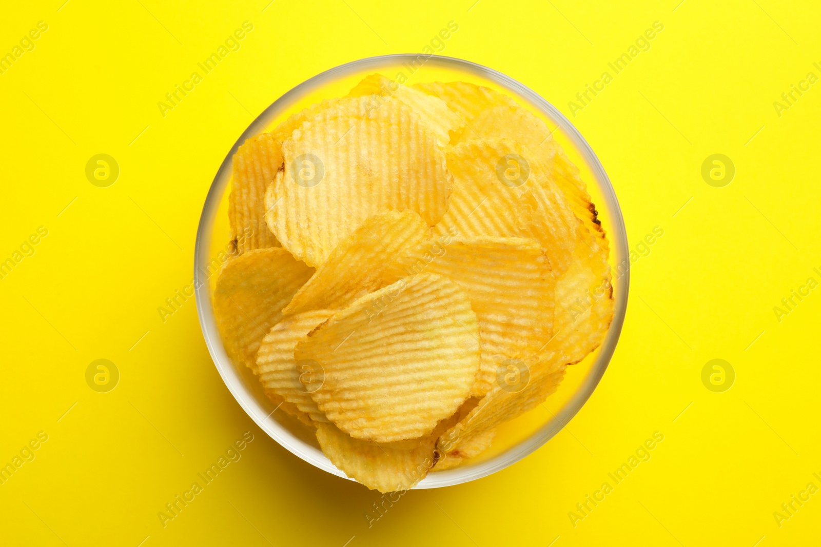 Photo of Delicious crispy potato chips in bowl on color background, top view