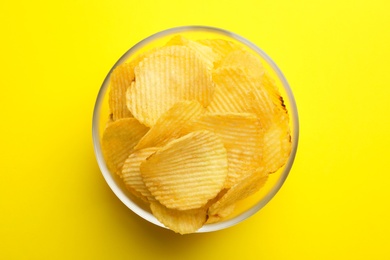 Delicious crispy potato chips in bowl on color background, top view