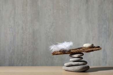 Photo of Stack of stones with tree branch and feather against grey background, space for text. Balance concept