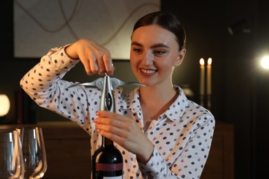 Photo of Romantic dinner. Happy woman opening wine bottle with corkscrew at home