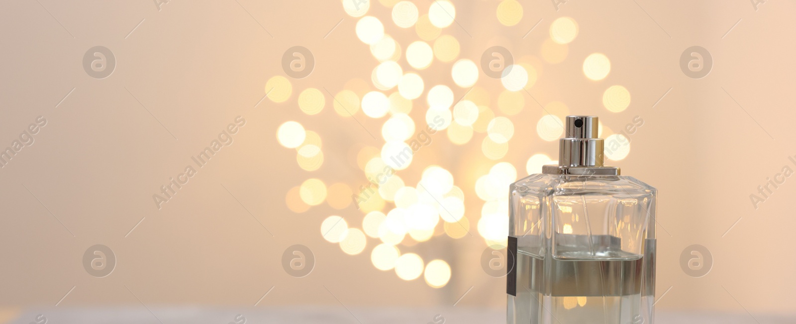 Photo of Bottle of perfume against beige background with blurred lights, space for text