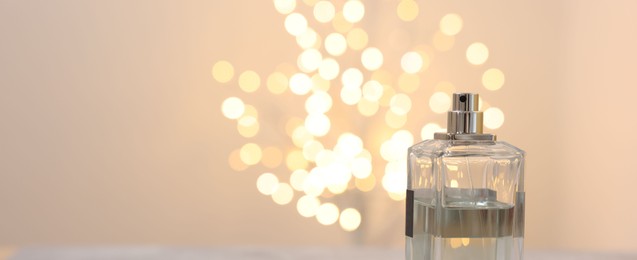 Photo of Bottle of perfume against beige background with blurred lights, space for text