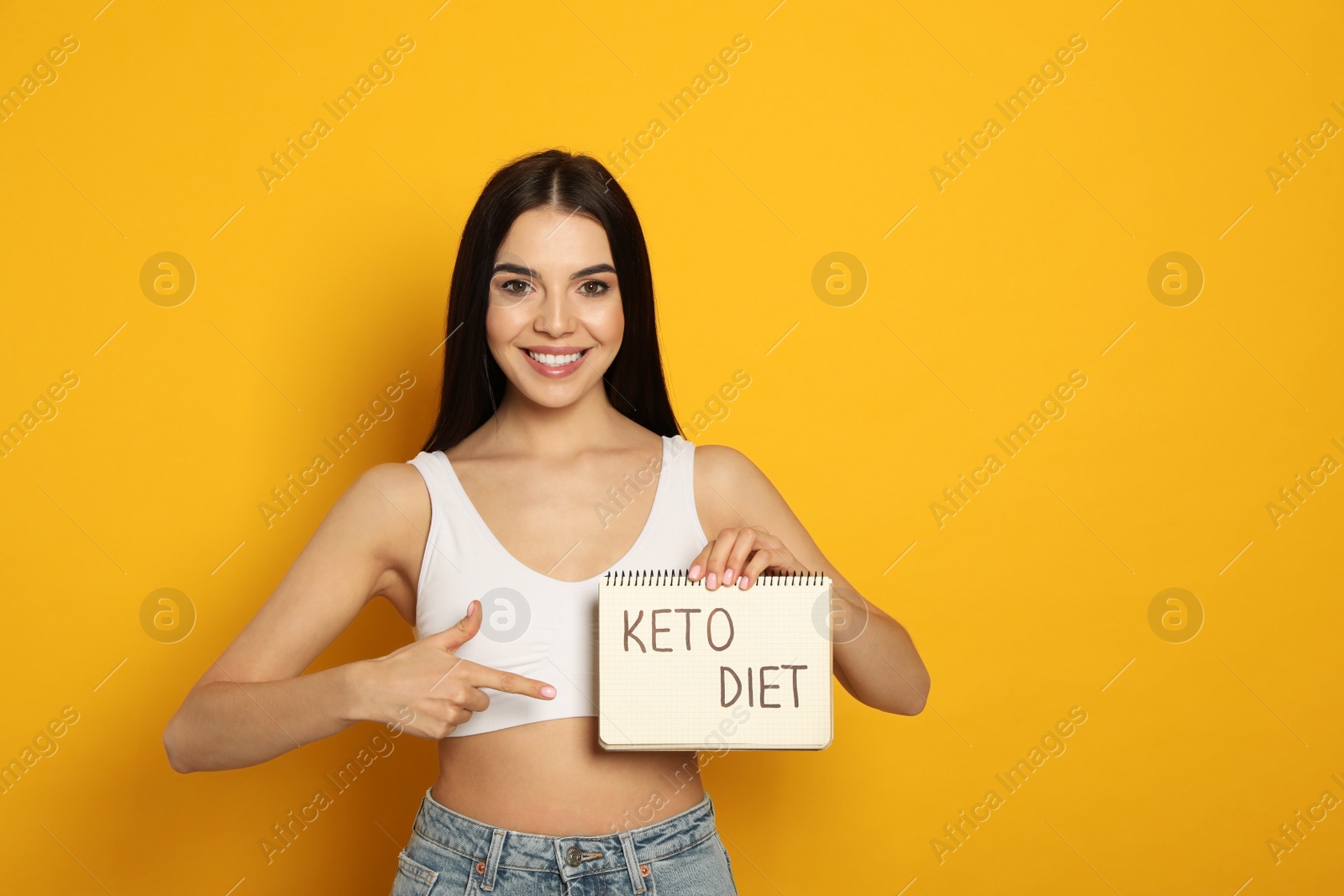 Photo of Happy woman holding notebook with words Keto Diet on yellow background. Space for text