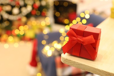 Red gift box on wooden shelf against blurred festive lights, space for text. Christmas celebration