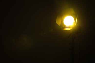 Photo of Bright yellow spotlight in darkness, space for text