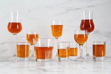 Photo of Different delicious liqueurs in glasses on white marble table