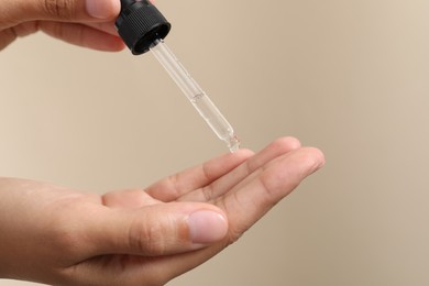Photo of Woman applying cosmetic serum onto her finger on beige background, closeup