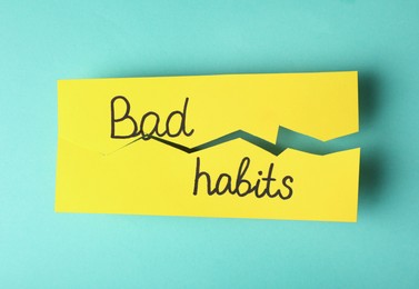 Photo of Torn paper with words Bad Habits on turquoise background, top view