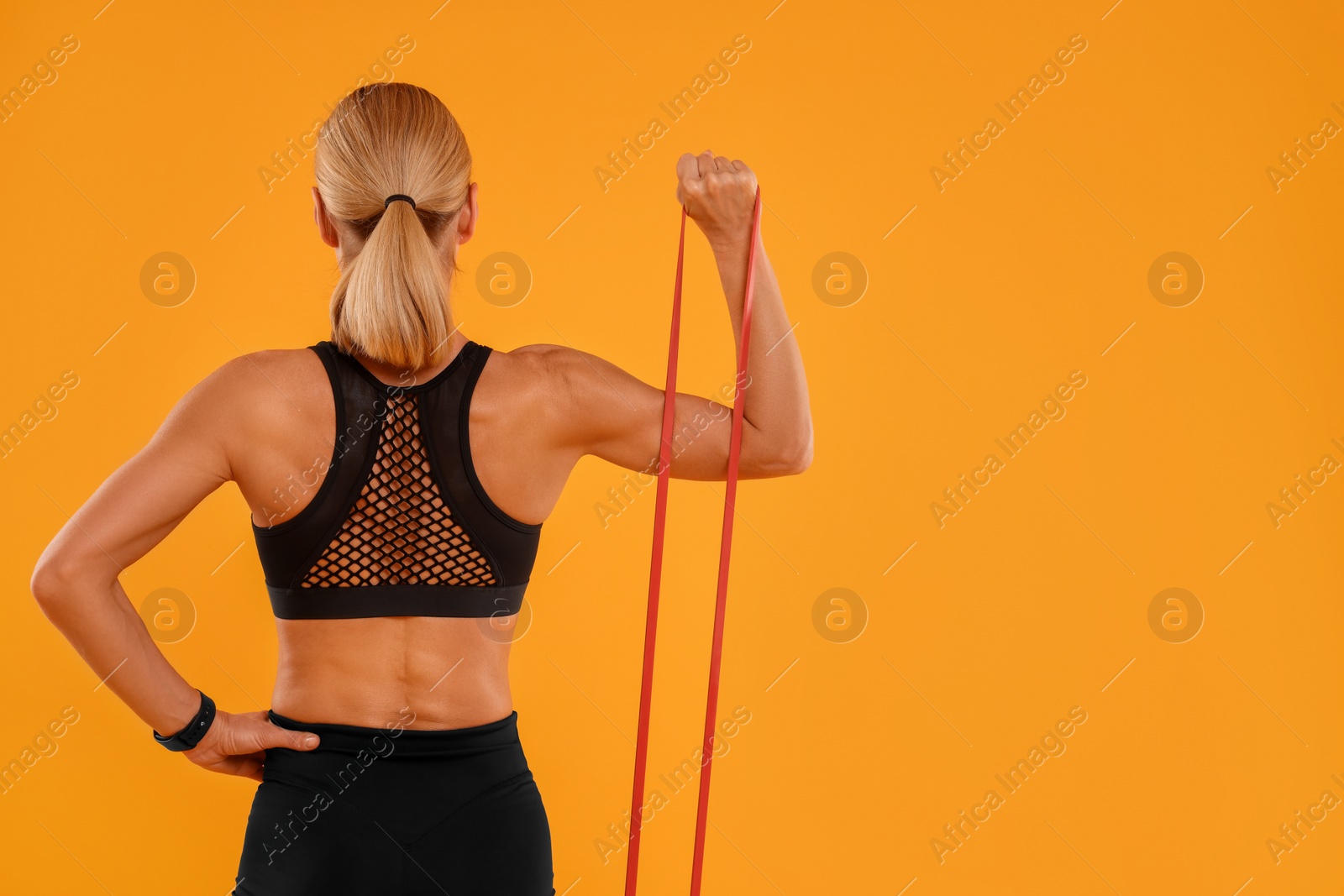 Photo of Woman exercising with elastic resistance band on orange background, back view. Space for text