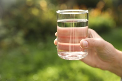 Photo of Woman holding glass of fresh water outdoors, closeup