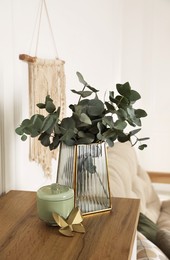 Photo of Stylish glass vase with eucalyptus branches and beautiful decor elements on wooden table indoors
