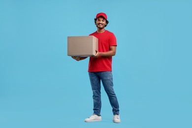Happy young courier with parcel on light blue background