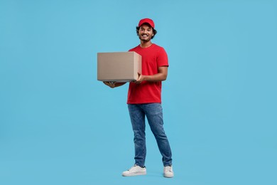 Photo of Happy young courier with parcel on light blue background