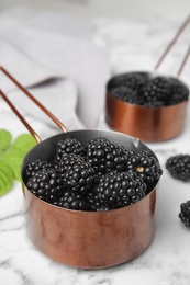 Photo of Metal saucepans with ripe blackberries on marble table