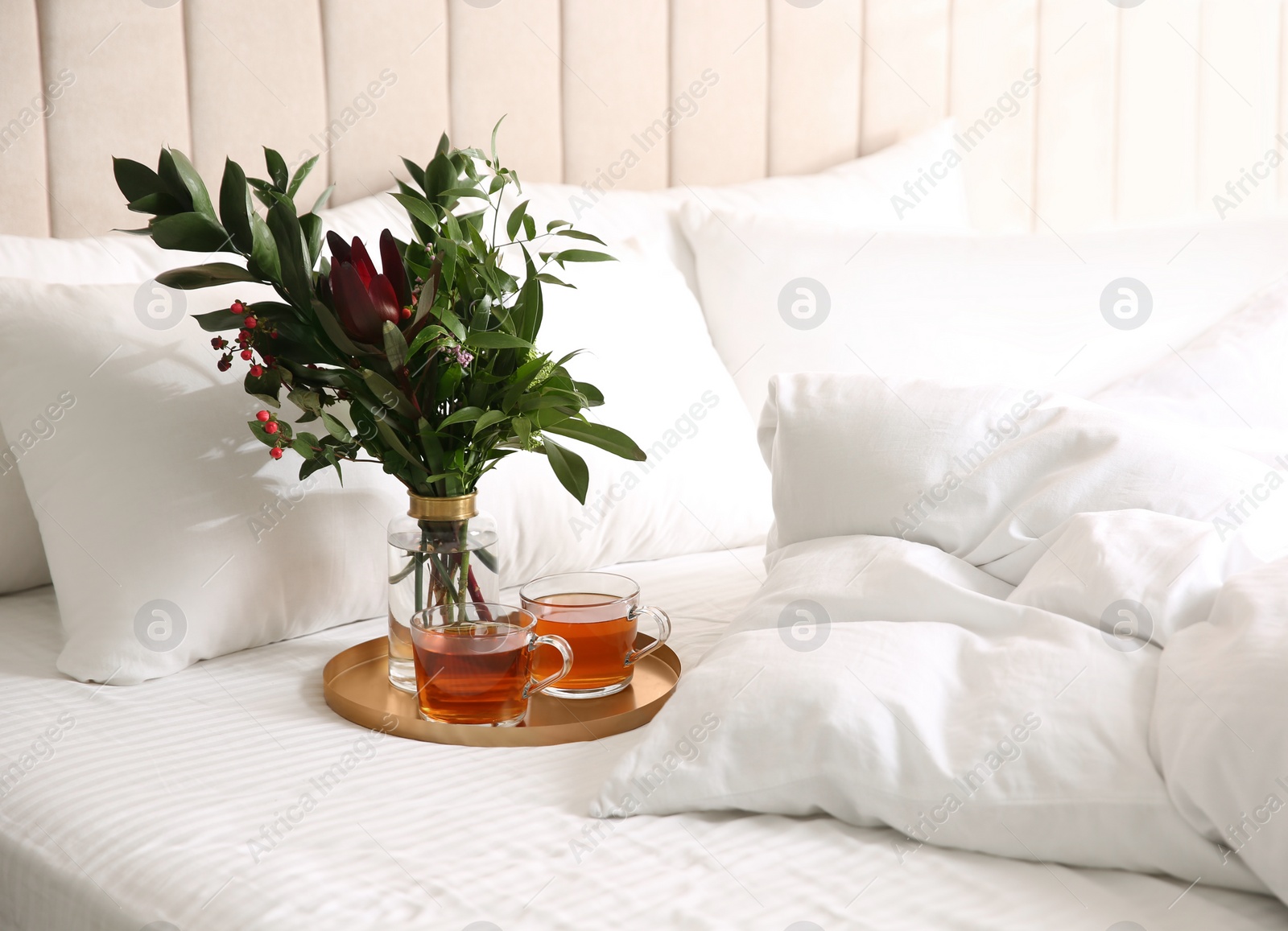 Photo of Tray with cups of tea and floral decor near soft blanket on bed