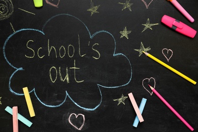 Photo of Pieces of color chalk and stationery on blackboard with text School's Out, flat lay. Summer holidays