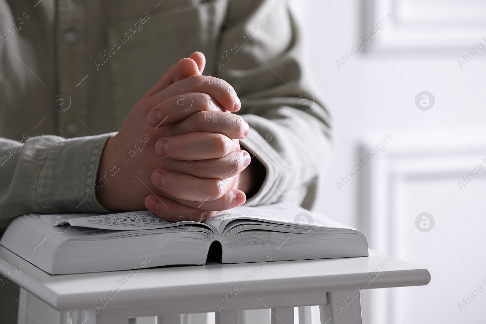 Photo of Religion. Christian man praying over Bible indoors, closeup