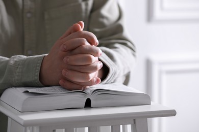 Religion. Christian man praying over Bible indoors, closeup