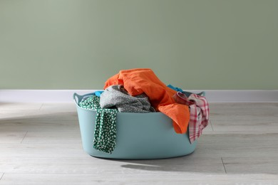 Laundry basket with clothes near light green wall indoors