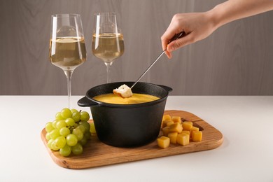 Photo of Woman dipping piece of bread into fondue pot with tasty melted cheese at white table, closeup