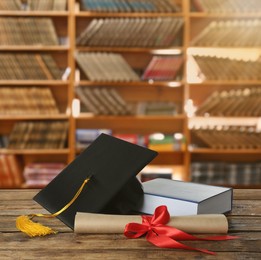 Image of Graduation hat, book and diploma on wooden table in library