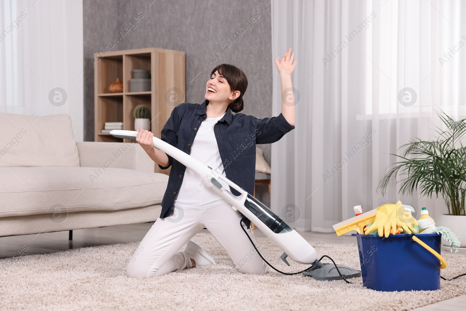 Photo of Happy young housewife having fun while cleaning carpet at home