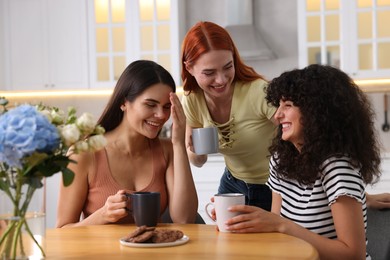 Photo of Happy young friends with cups of drink spending time together in kitchen