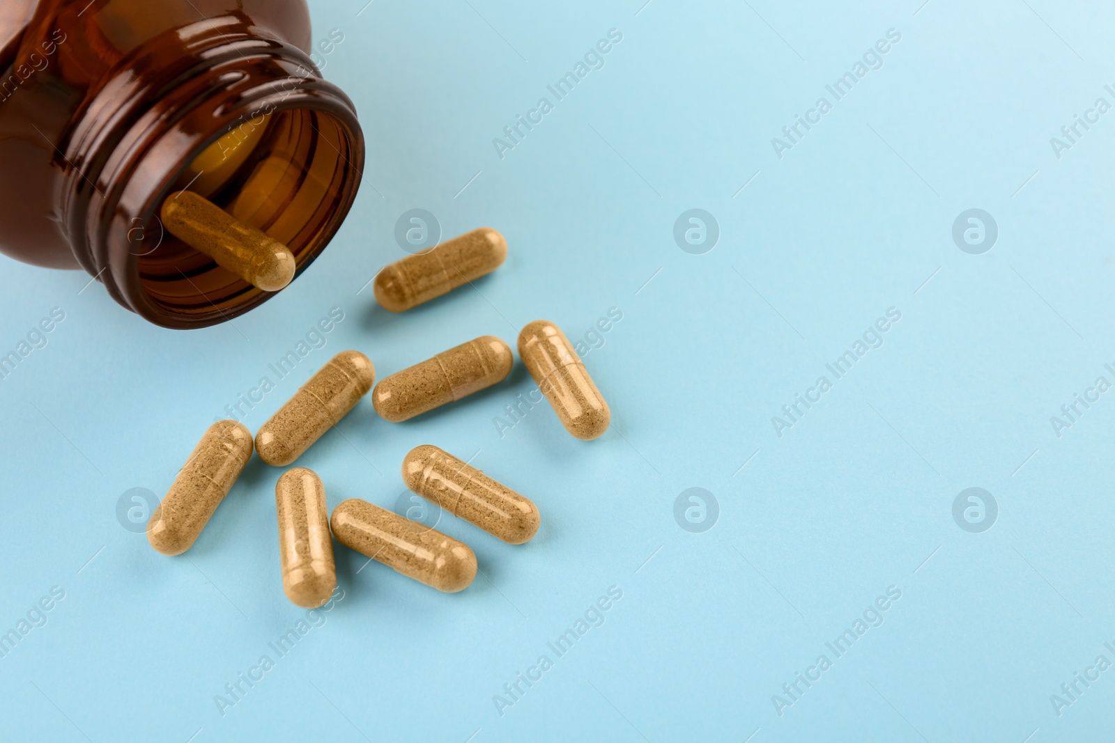 Photo of Bottle and vitamin capsules on light blue background, closeup. Space for text