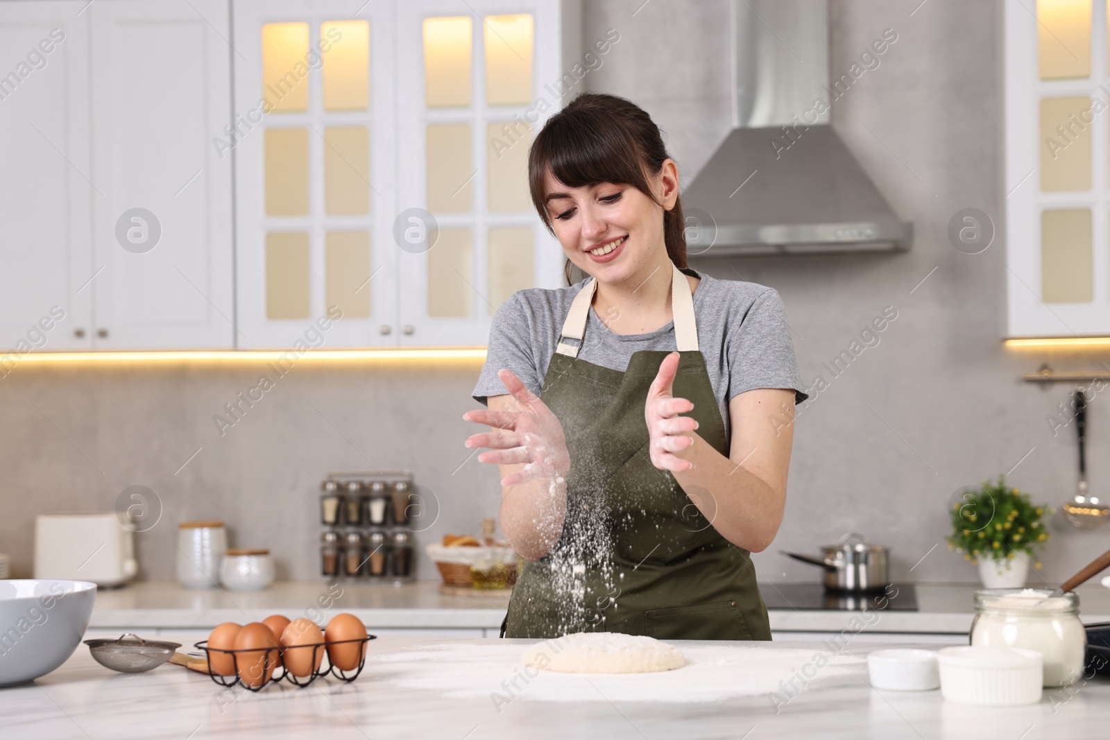 Photo of Happy young housewife making dough at white marble table in kitchen