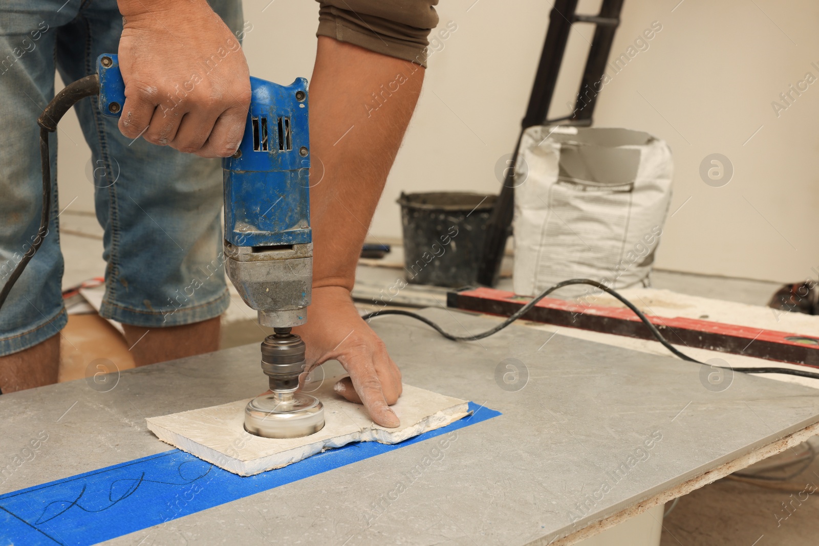 Photo of Worker making socket hole in tile indoors, closeup