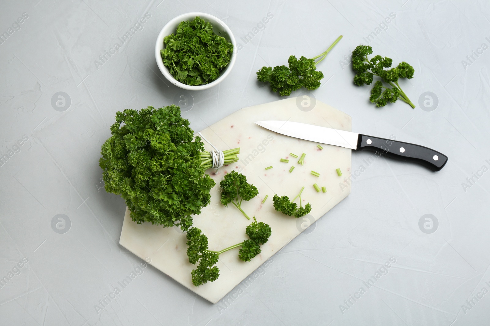 Photo of Fresh curly parsley, cutting board and knife on light grey table, flat lay