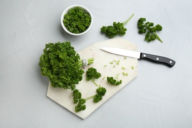 Photo of Fresh curly parsley, cutting board and knife on light grey table, flat lay