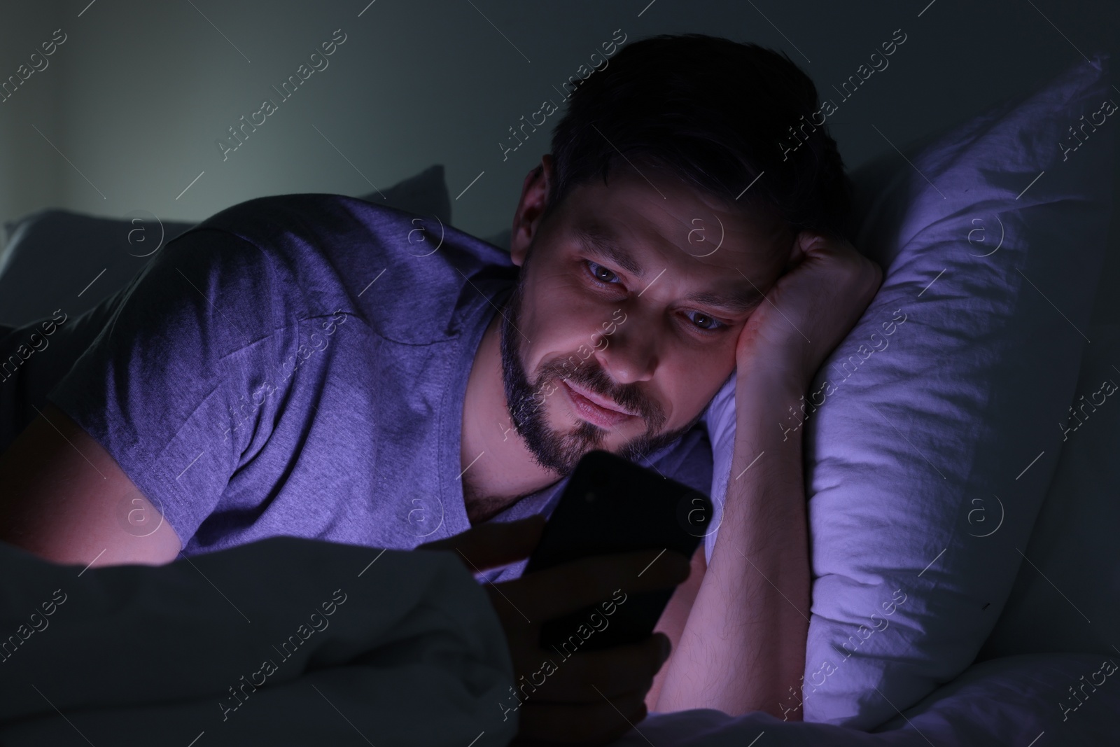 Photo of Man using smartphone in bed at night. Internet addiction