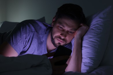 Photo of Man using smartphone in bed at night. Internet addiction