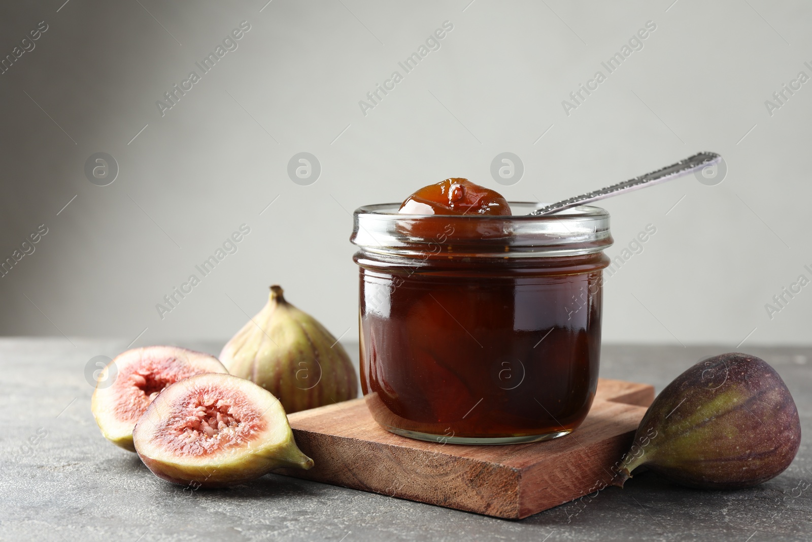 Photo of Jar of tasty sweet jam and fresh figs on grey table