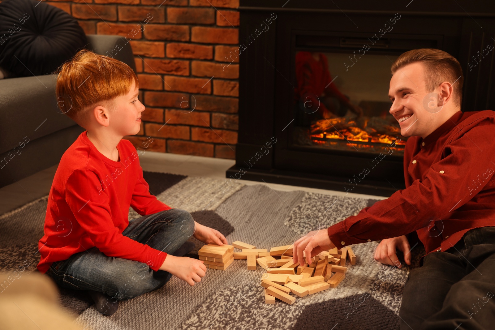 Photo of Happy father and son playing together on floor near fireplace at home