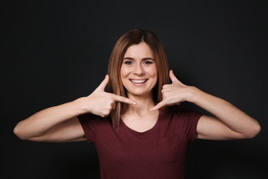 Photo of Woman showing CALL ME gesture in sign language on black background