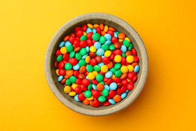 Photo of Bowl with tasty colorful candies on yellow background, top view