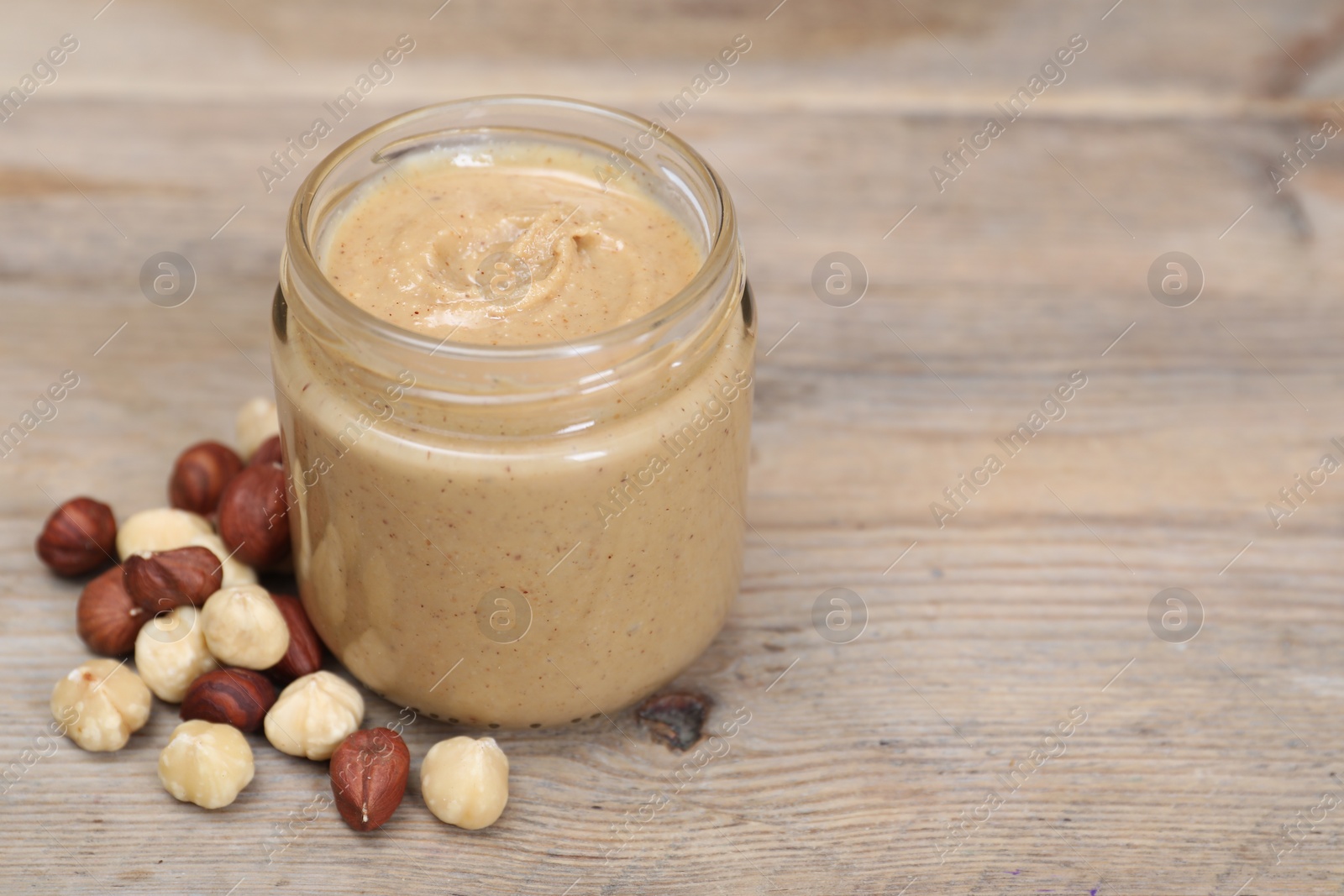 Photo of Tasty nut paste in jar and hazelnuts on wooden table, closeup. Space for text