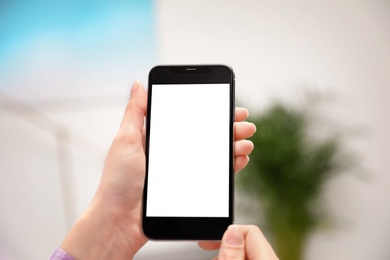 Woman holding smartphone with blank screen indoors, closeup of hands. Space for text