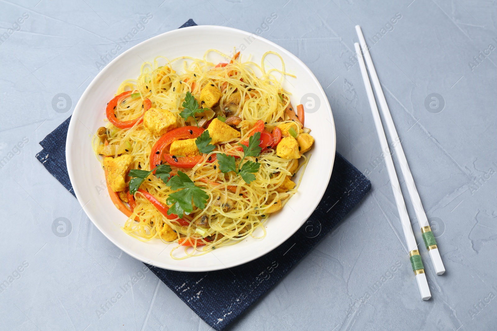 Photo of Stir-fry. Delicious cooked noodles with chicken and vegetables in bowl served on gray textured table, flat lay